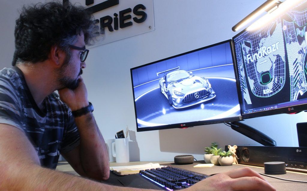 A person looking at a computer with an image of a car on one screen and graphics on the other.