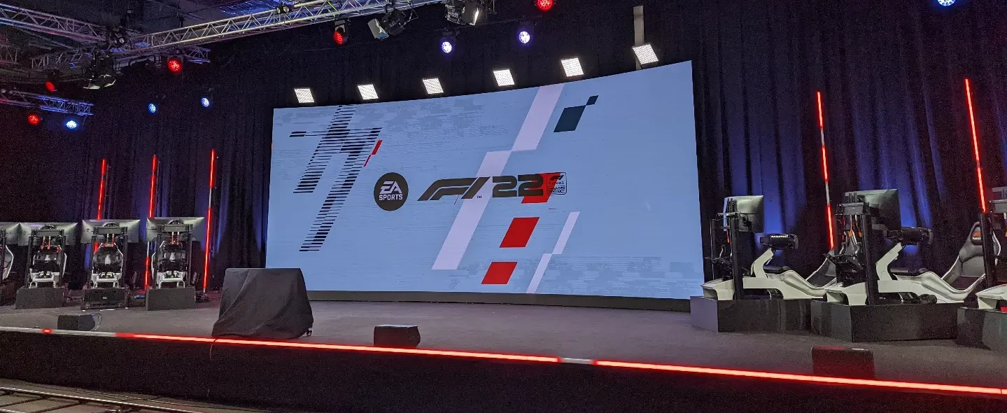 A line of sims on a stage with a screen that has the F1 22 logo.