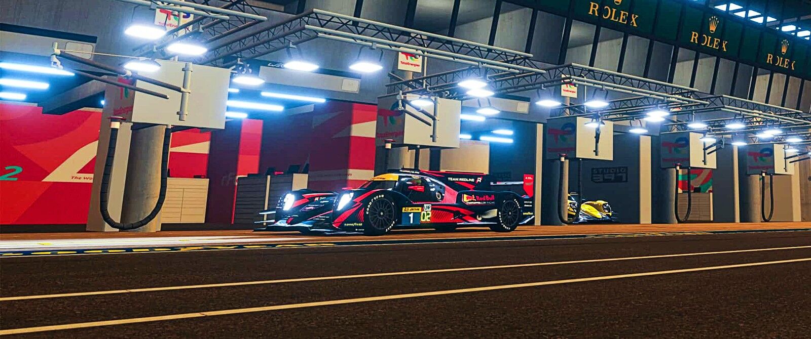 An Oreca 07 in a pitbox at the Circuit de la Sarthe during the night with lights illuminating the surrounding area.