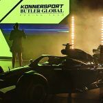 A dim studio with silhouettes of people and an F1 car, with a yellow sign reading Konnersport Butler Global Racing Team above.