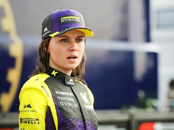 A woman in the paddock area of an F1 Grand Prix wearing a purple and yellow cap with black and yellow overalls.