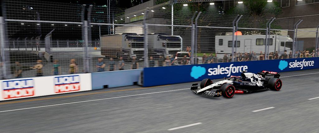 A white and dark blue F1 car racing by a cordoned off piece of street track at night