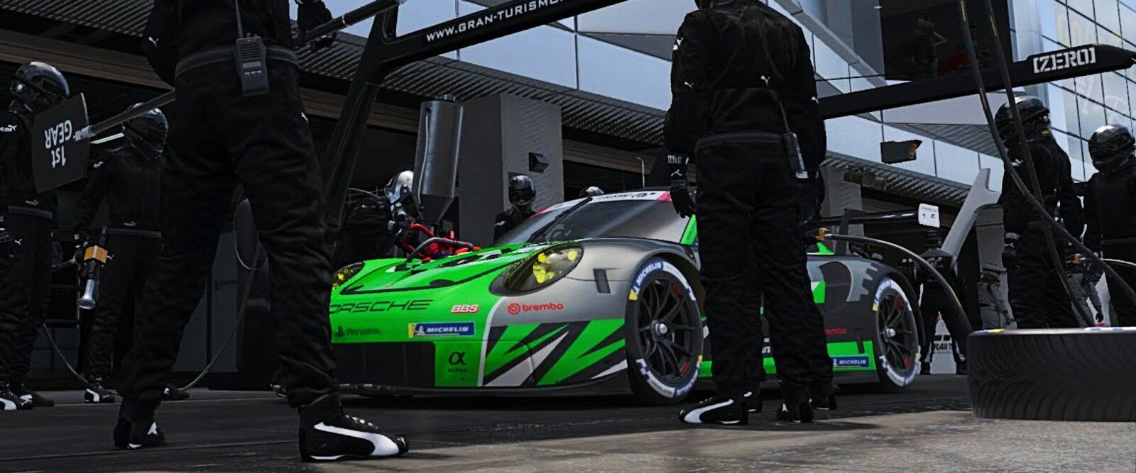 A green and dark silver Porsche being serviced in the pit box.