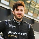 A brown haired man with a beard wearing black racing overalls.