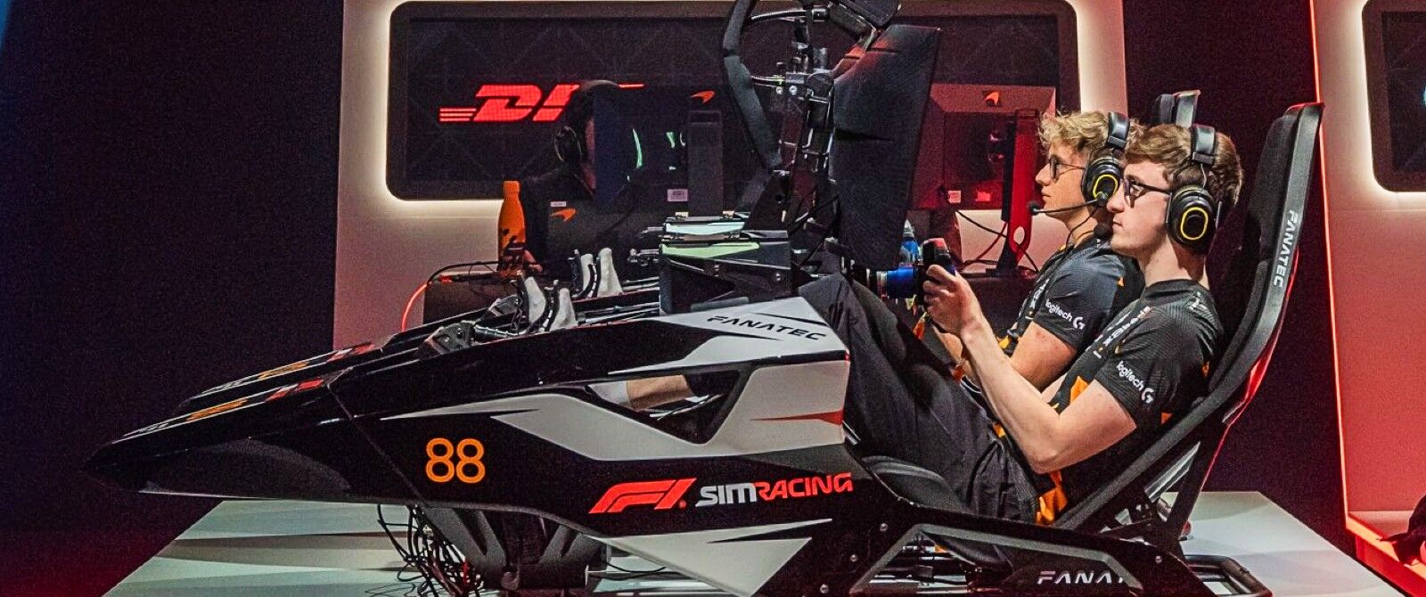 A sim racing setup with two people sat in rigs, one behind the other.