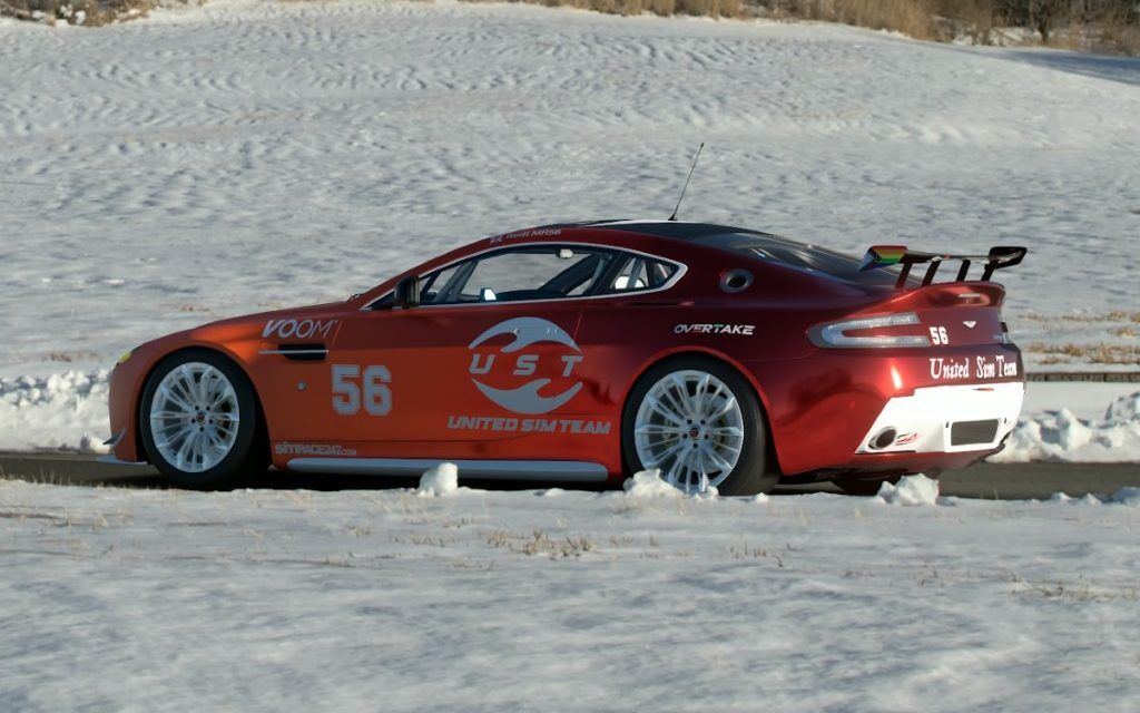 A red coloured Aston Martin racing car on a road surrounded by snow.